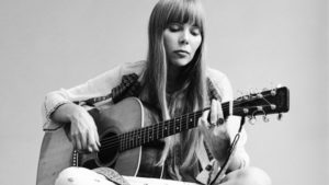 Portrait of Canadian musician Joni Mitchell seated on the floor playing acoustic guitar, November 1968. This image is from a shoot for the fashion magazine Vogue. Mitchell wears a loose-fitting white dress. (Photo by Jack Robinson/Getty Images)
